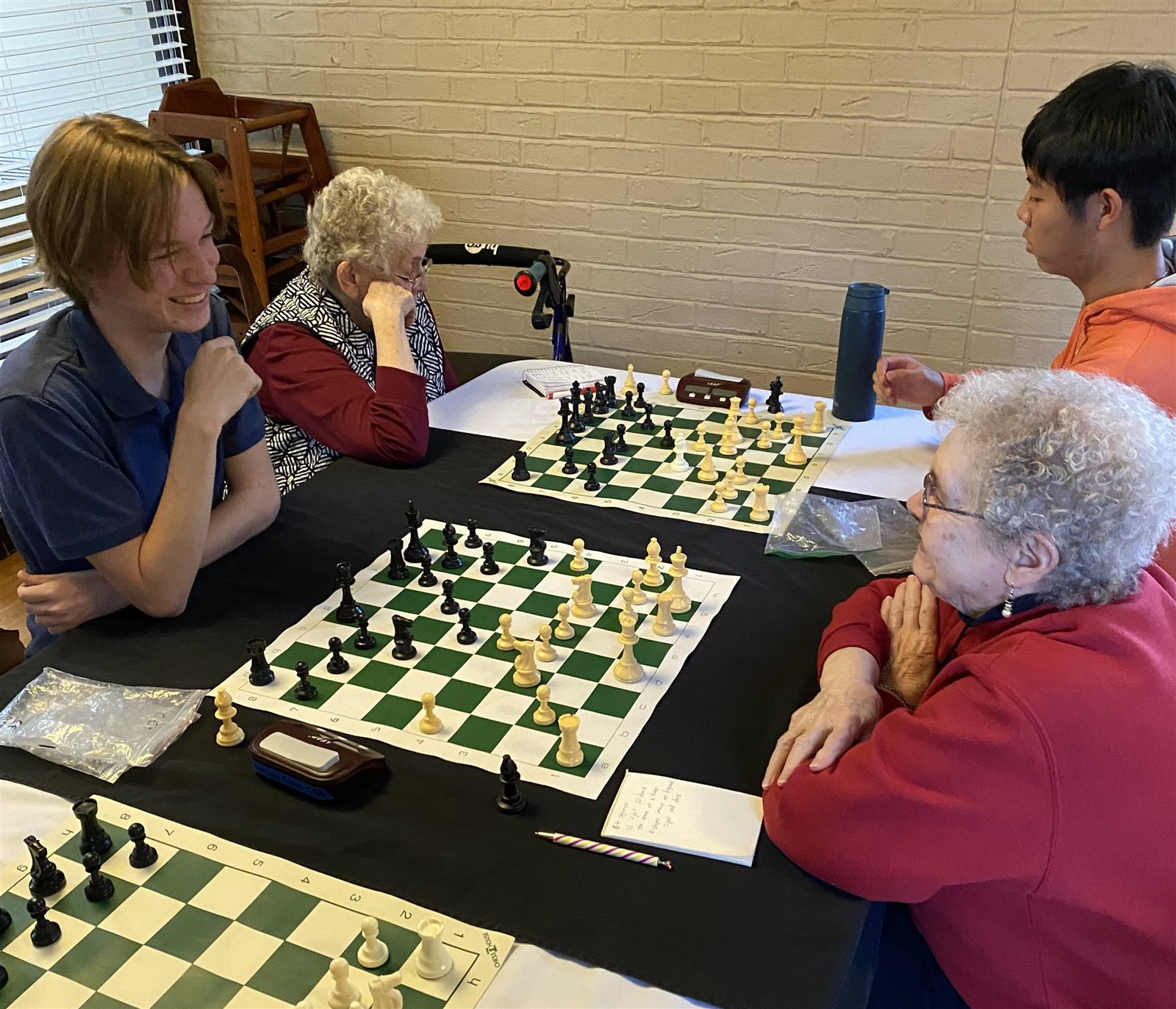 Students and seniors playing chess together across several boards